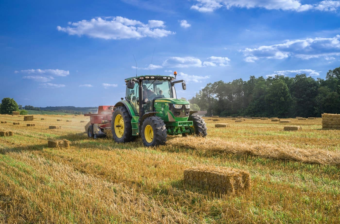 Green tractor baling a harvested field under a blue sky