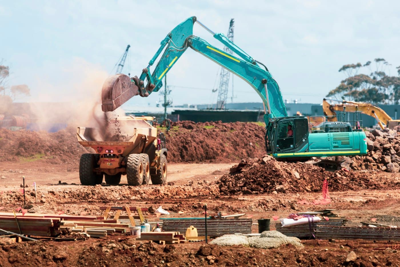 Excavator tipping soil into an articulated dump truck on an earthworks site