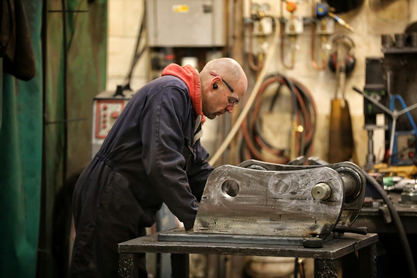 Engineer in overalls and safety glasses repairing a heavy steel excavator coupler