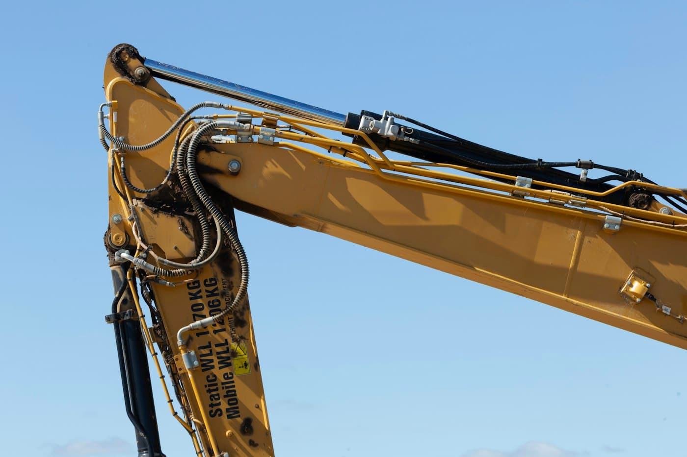 Excavator boom with hydraulic rams and hose runs against a blue sky